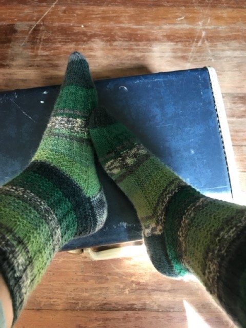 A pair of socks I knitted up during a week of being a summer camp counselor in 2016. The socks have an all-over broken rib texture, and are striped in different shade of green and grey.