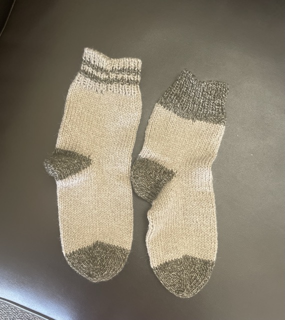 A pair of socks in brownish-grey with greenish-grey accents, made with alpaca yarn for a soft and cozy slipper-sock experience. Knitted in 2020.