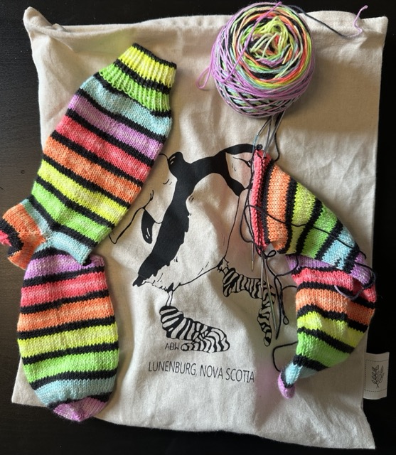 One finished sock and one sock-in-progress, being worked up in a self-striping fluorescent rainbow yarn.